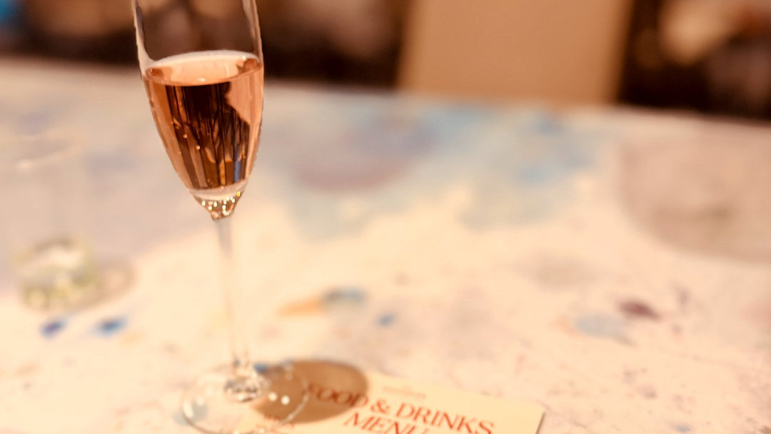 Champagne flute beside the Paint Juicy food and drinks menu on a paint-splattered table at Currumbin RSL Paint and Sip