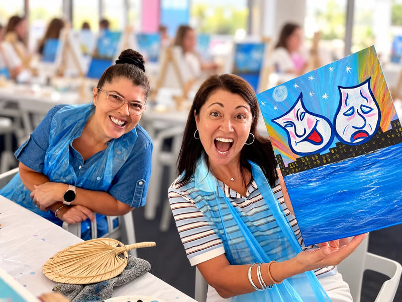 Two guests grinning beside a finished canvas under neon lights at a Hervey Bay Paint Juicy night