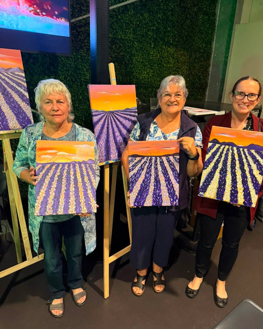 Paint Juicy guests holding their finished Lavender Fields paintings at a paint and sip night, photo 3 of 5