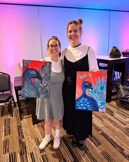 Paint Juicy guests holding their finished The Red Peacock paintings at a paint and sip night, photo 1 of 4