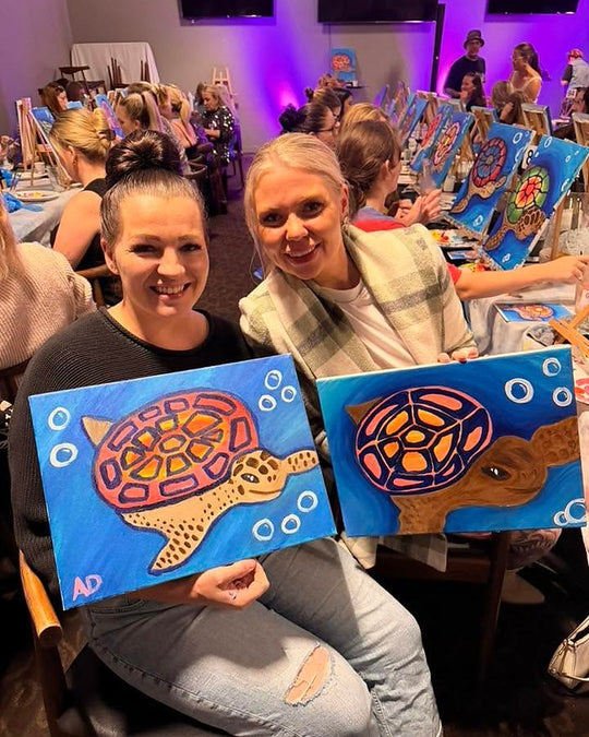 Paint Juicy guests holding their finished Sea Turtle paintings at a paint and sip night, photo 1 of 6