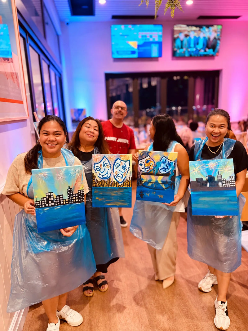 Four friends in aprons holding their finished fireworks and theatre mask canvases at a Townsville paint and sip